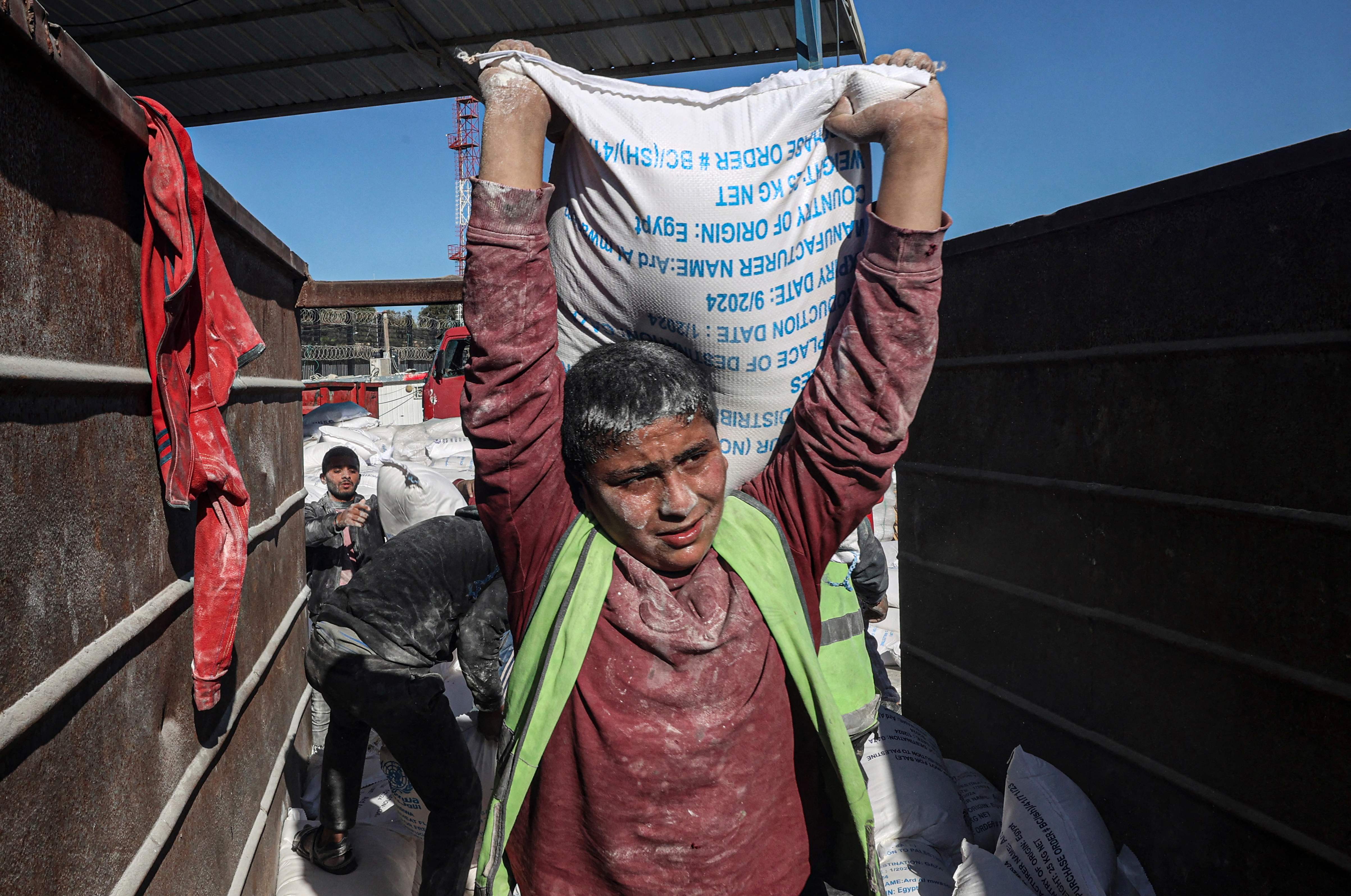 Des ouvriers déchargent des sacs d'aide humanitaire entrant dans Gaza, le 17 février 2024 (Photo Said KHATIB / AFP)