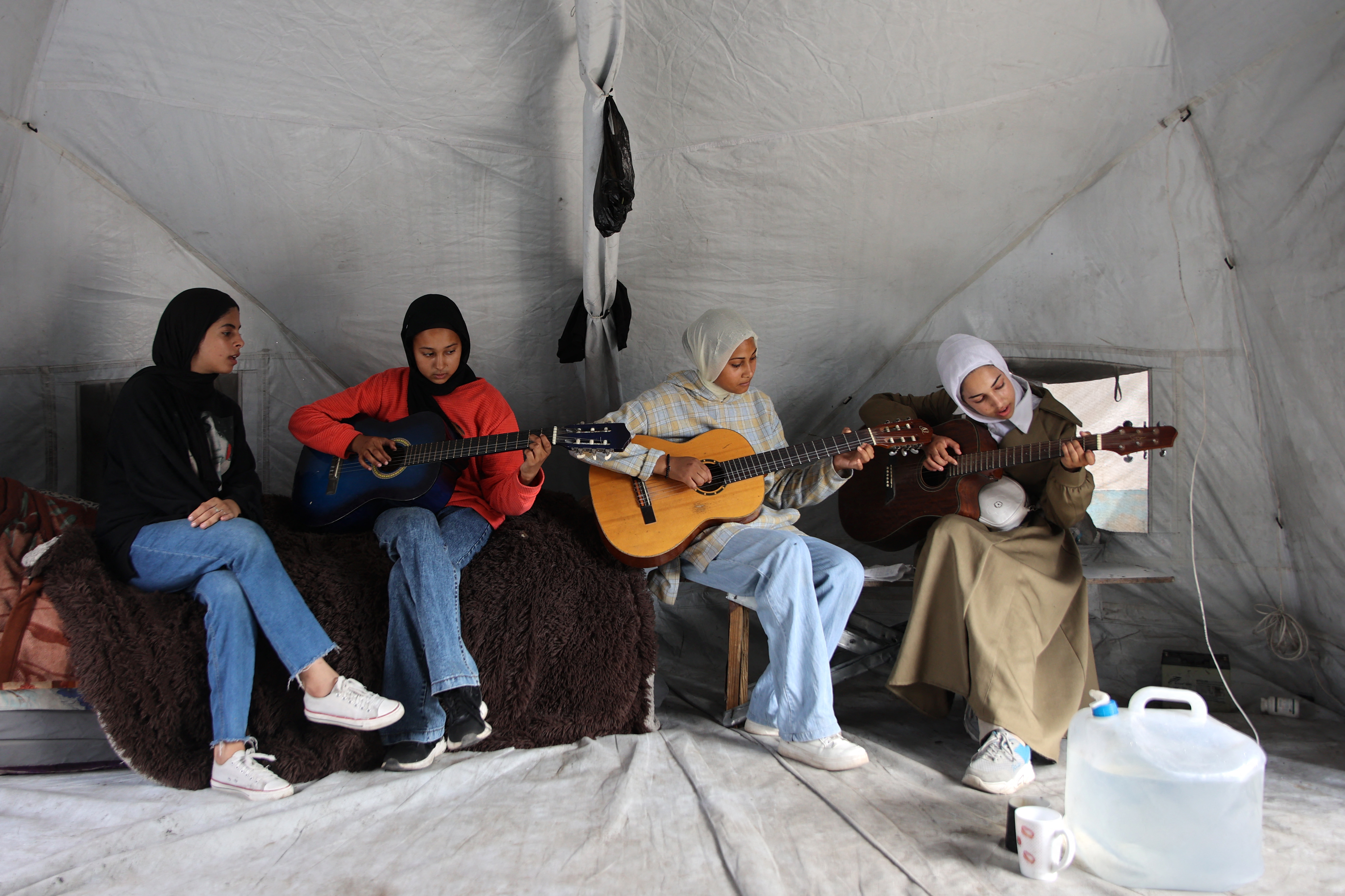 Gathered together over the blanketed earth, these three young guitar players and a singer are among many budding musicians across Gaza, where, according to several reports over the last 21 months of war, teachers have taken up their instruments to bring music into a world of violence. (Credit: Omar al-Qattaa/AFP)